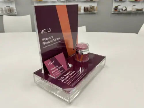 Clear Acrylic Counter Riser With Printed Backer Displaying Vella Skincare Products